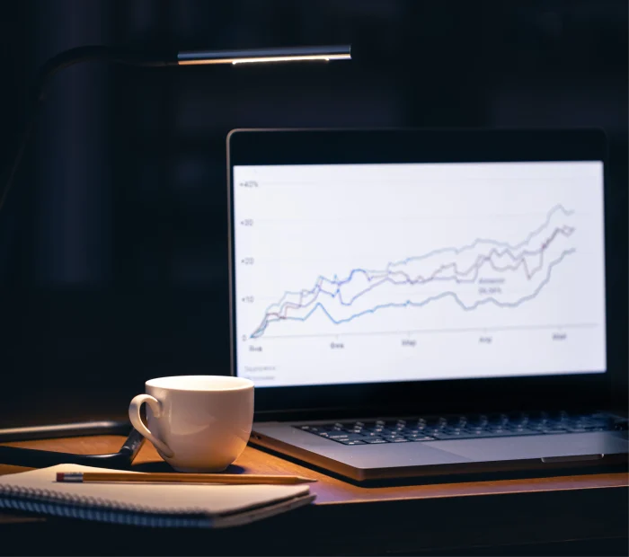 Dark room with laptop showing financial growth chart and warm desk lamp
